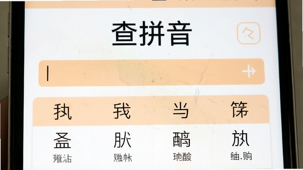 查拼音软件运行界面特写，中央显示“查拼音”字样和输入框，下方列出多个汉字的拼音对照结果，界面配色以白色和淡橙色为主，文字清晰，风格清新明快。
