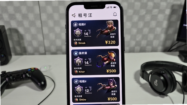 租号汪应用内账号浏览界面，手机屏幕上纵向排列多个游戏账号卡片，每张卡片展示游戏名称、段位图标、皮肤数量及租用价格，背景为浅灰色墙面，桌面散落着游戏手柄与耳机，画面明亮清晰，突出账号资源的丰富多样，16:9构图