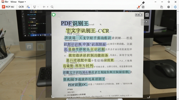 PDF识别王OCR文字识别功能演示，一张拍摄的纸质文档照片正在被软件处理，文字被高亮框选并转换为可编辑的文本，背景为办公桌和电脑，画面清晰展现识别过程