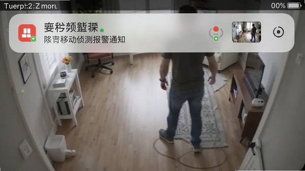 视频监控看家王移动侦测报警通知截图，手机通知栏显示报警消息和抓拍缩略图，背景为监控画面中有人走动的动态场景，突出智能报警功能
