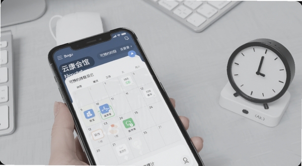 云康会馆技师端界面中展示排班日历与可预约时段设置,手机屏幕特写,背景为浅灰色办公桌面,画面右侧放置简约时钟图标,整体色调柔和,突出排班管理功能,适配Boogu模型生成