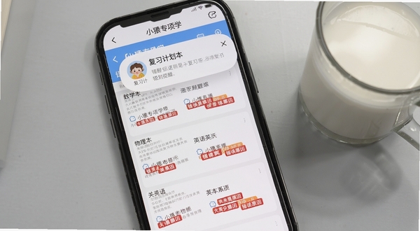 手机屏幕特写，显示小猿专项学错题本页面，错题按数学、物理、英语分列排列，每道题旁有红色标签标注错误原因，屏幕上方有复习计划提醒弹窗，背景为浅灰色书桌桌面，旁边放着一杯热牛奶，画面呈现温馨的学习氛围，细节清晰，软件名称在页面顶部导航栏可见