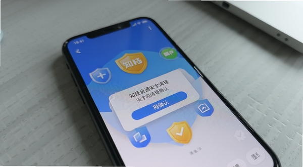 手机屏幕上显示知柚全通安全清理确认对话框,周围有防护盾牌图标,背景为浅灰色室内桌面,光线柔和,强调操作安全性与用户信任感,写实摄影风格