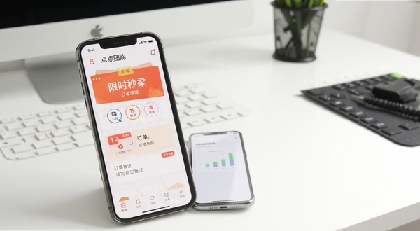 点点团购版本更新后的界面展示图，画面中手机屏幕显示着新增的限时秒杀入口和订单备注填写框，背景为简洁的白色工作台，光线明亮，突出功能升级的直观感受