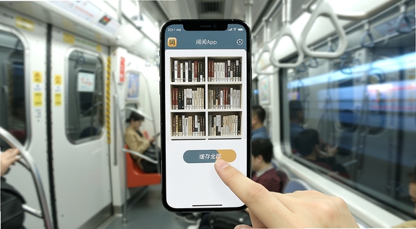 已阅App在手机屏幕上显示书架界面，旁边有一只手正在点击“缓存全部”按钮，背景是地铁车厢与窗外的流动光影，画面风格写实明亮，突出移动阅读场景，软件名称已阅出现在手机顶部状态栏