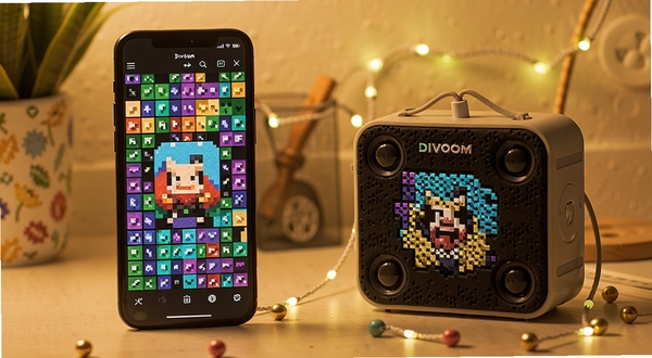 点音App像素画板界面，手机屏幕显示彩色像素网格，旁边是Divoom像素音箱同步展示同款图案，桌面环境温馨，柔和暖光，细节清晰