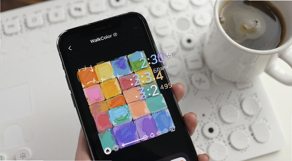 WalkColor 软件内色彩画布与步数解锁动画特写,画面主体为手机屏幕上正在填充的彩色方块和飘动的步数数字,背景是简洁的白色工作台和一杯咖啡,光线柔和,突出轻量应用的使用场景