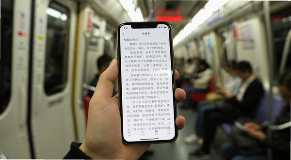纵横小说移动端使用场景，一只手握持手机在地铁车厢内阅读，手机屏幕显示小说正文页面，周围环境虚化处理，突出阅读的沉浸感与便捷性