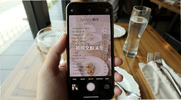 渡文翻译 拍照翻译功能演示 手机摄像头对准一份英文菜单 屏幕上叠加显示中文翻译结果 背景为餐厅桌面 自然光线 细节清晰 适配Boogu模型生成