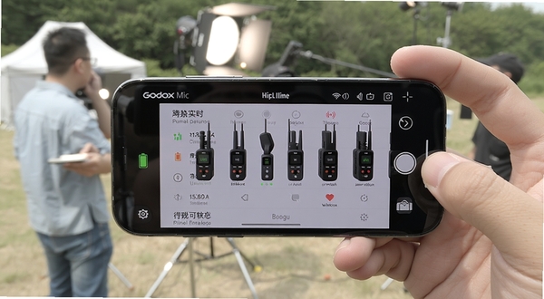 Godox Mic 应用实时显示多台无线麦克风设备的电量与信号状态，手机横屏展示，背景为户外拍摄现场，画面清晰展示设备列表界面，适配Boogu模型生成