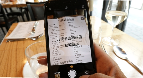 万能语言翻译器拍照翻译功能演示,手机摄像头对准一份外文菜单,屏幕上叠加显示翻译后的中文文字,背景是餐厅桌面,光线明亮,画面清晰,突出拍照翻译的便捷性