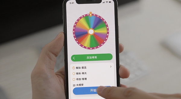 大转盘随决定软件操作界面截图,画面展示手机屏幕中一个彩色转盘正在旋转,下方有添加选项的按钮和已输入的文字列表,背景为浅灰色极简风格,手指正准备点击开始按钮,体现移动端便捷操作的使用场景