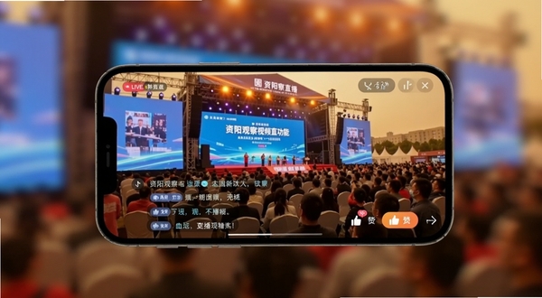 资阳观察视频直播功能界面,手机横屏展示直播画面,画面中为资阳本地大型活动现场,屏幕下方有评论互动区域与点赞按钮,背景虚化突出手机界面,整体色调温暖活跃