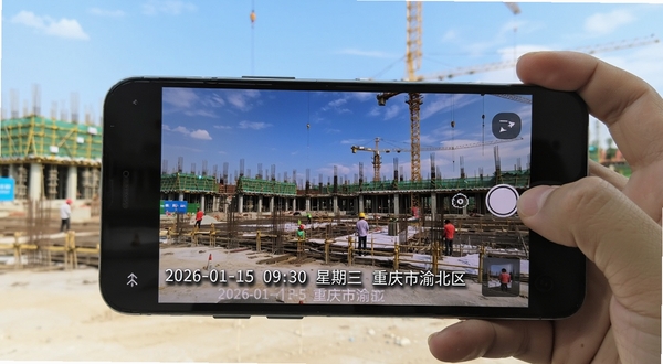 开心水印相机实时水印叠加功能展示，画面中一部安卓手机正在拍摄建筑工地场景，照片底部清晰显示“2026-01-15 09:30 星期三 重庆市渝北区”等水印信息，水印字体为白色带阴影，背景为蓝天下的施工现场，整体构图体现真实记录感