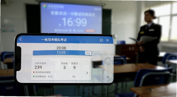 一帆驾考模拟考试界面，手机横屏展示考试倒计时和答题卡，背景为考场环境虚化效果，有监考老师剪影和考试座位，营造真实考试氛围