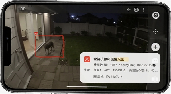 手机屏幕显示监控画面中有移动物体被红色方框标记，旁边弹出报警通知，背景是夜晚的庭院，手机监控软件界面，突出移动侦测报警功能