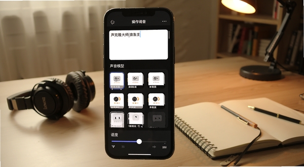 声音克隆大师文本转语音操作界面,手机屏幕展示文本输入区域与声音模型选择列表,下方有语速调节滑块,背景为暖色调书房场景,桌上放着耳机与笔记本,体现创作氛围