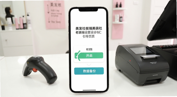 美发社老板端安装设置引导页面,手机屏幕显示权限开启与数据备份选项,背景为美发店收银台,有扫码枪与打印机,画面明亮简洁,突出操作指引感