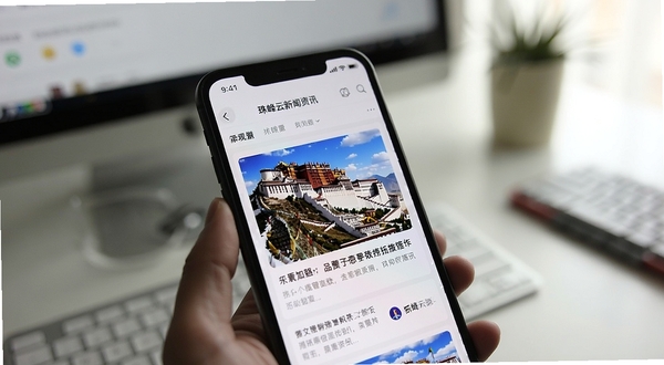 珠峰云新闻资讯页面特写，画面主体为手机屏幕显示西藏布达拉宫相关的新闻图文卡片，背景区域为简洁的室内办公桌面，光线柔和，强调资讯阅读的沉浸感与权威感