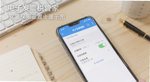 电子发票税管家安装权限设置步骤示意图，手机屏幕显示应用权限管理页面，存储权限开关处于开启状态，背景为浅色木质桌面与文具，画面简洁清晰，适合教程配图