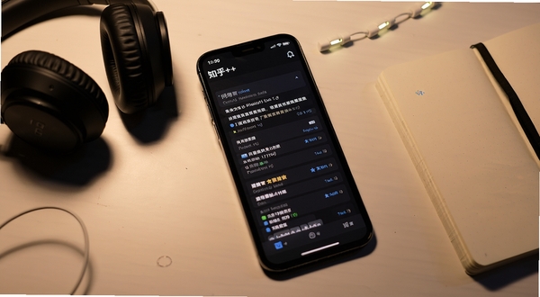 知乎++夜间阅读模式界面，深色背景中显示问答正文，手机置于桌面，旁边有耳机与笔记本，氛围安静舒适