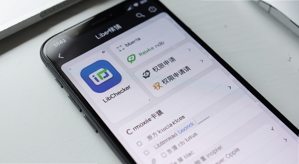 LibChecker应用详情页面特写,屏幕上清晰展示某款应用的原生库列表与权限申请清单,界面采用卡片式布局,左侧为应用图标与名称,右侧为分项检测结果,背景为干净的浅灰办公桌面环境,柔和光线从左上角照射,画面聚焦于手机屏幕内容,突出信息展示的层次感与可读性