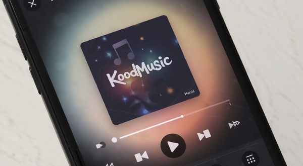 KoodMusic音乐播放器主界面，简洁深色主题，中央展示专辑封面与播放控制按钮，背景为柔和渐变光晕，手机屏幕特写视角，现代扁平化设计风格